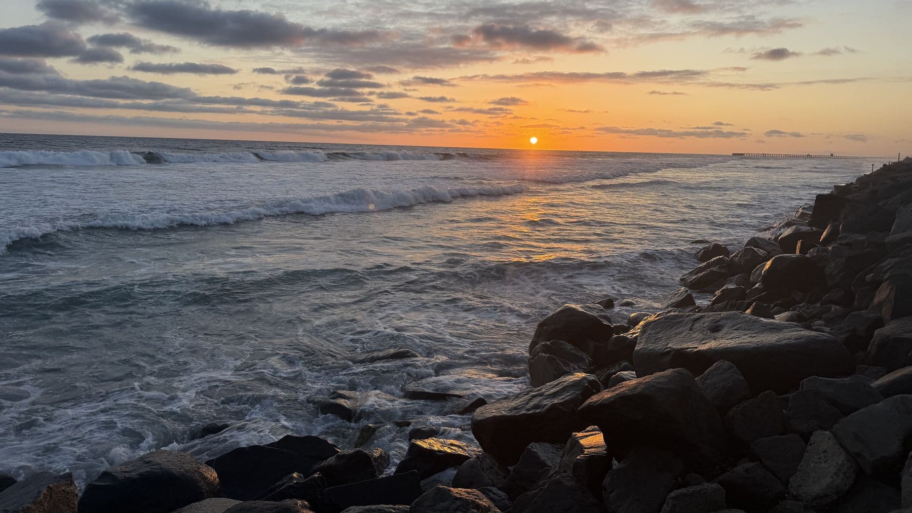 The sun going down over the ocean, waves breaking on dark rocks