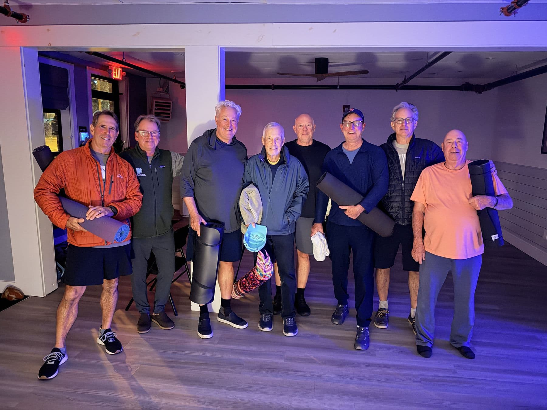 Eight guys holding rolled-up mats, grinning after class